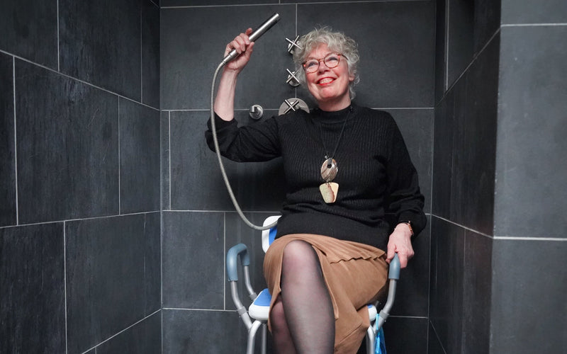 Vrouw zit lachend op de Safe Age douchestoel onder de douche